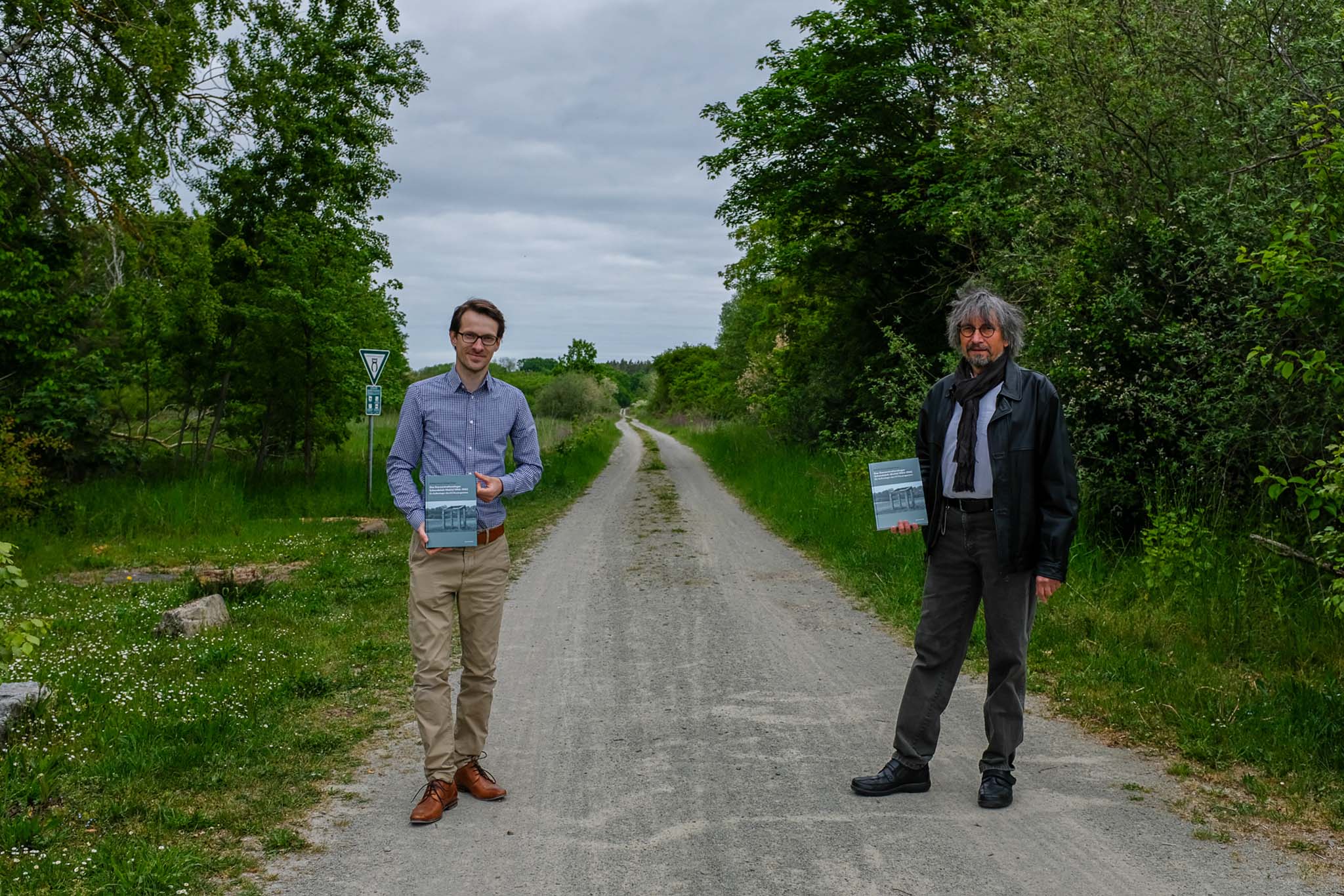 Zwei Personen stehen am WEg zum KZ Schandelah-Wohld. Sie halten jeweils ein Buch in der Hand. Es sind Benedikt Einert und Diethelm Krause-Hotopp.